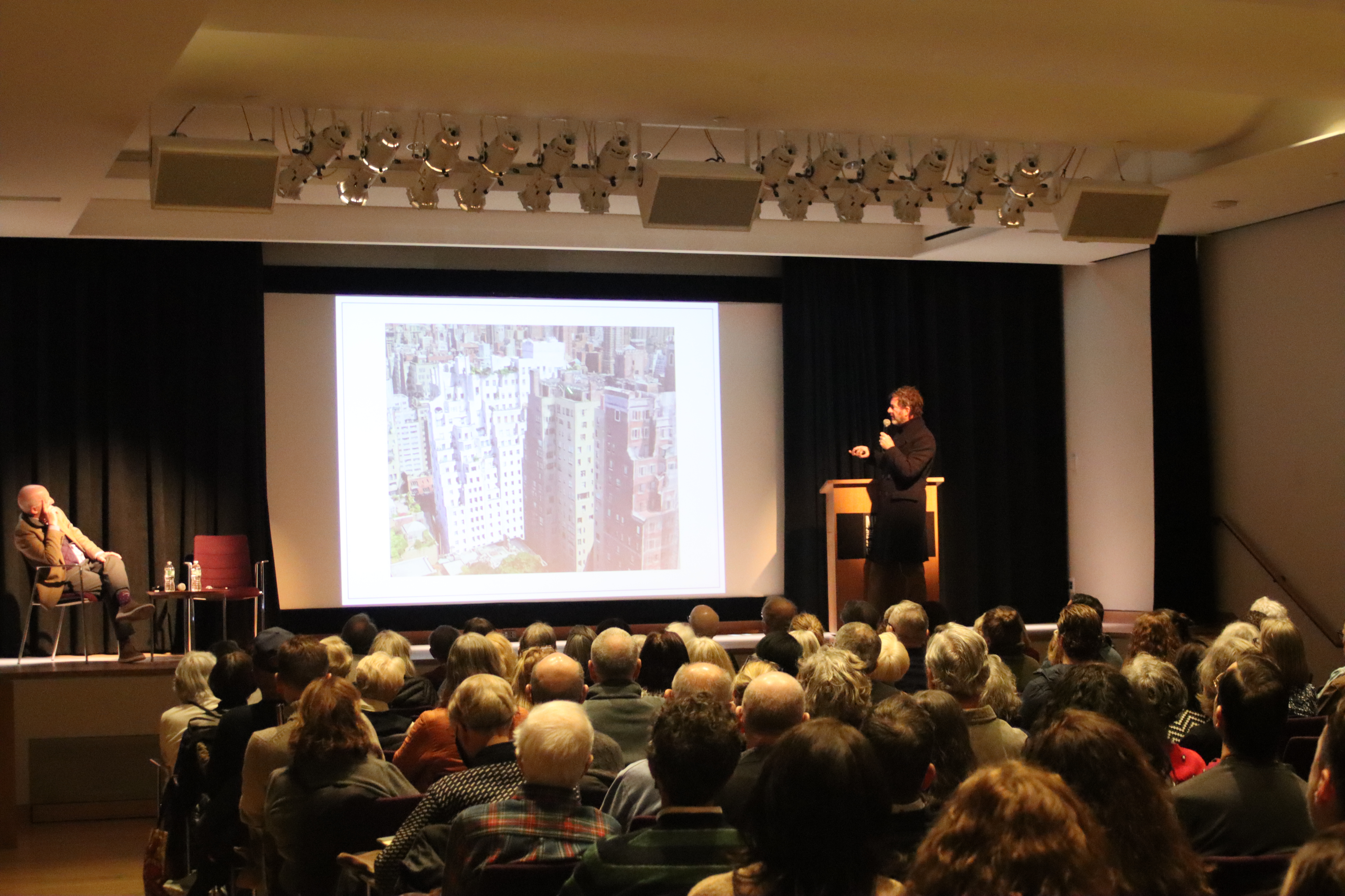Two men giving a presentation on New York City architecture to a large audience